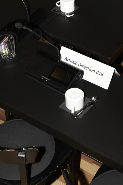 Ein Tisch von oben fotografiert. Auf dem Tisch steht ein Kaffee-Gedeck, ein Mikrofon und das Platzschild "Artistic Direction d16"