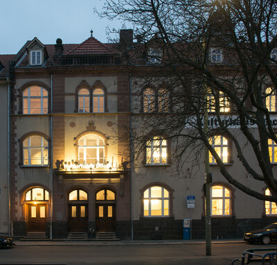 Exterior view of the Kulturhaus Dock 4, where the documenta archiv has its premises. The windows are brightly lit.