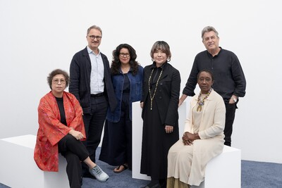 Two people sit on white stools, with four other members of the search committee positioned behind them.