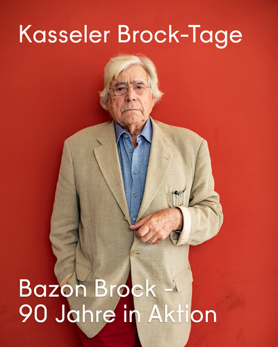 Bazon Brock im hellen Jackett vor rotem Hintergrund