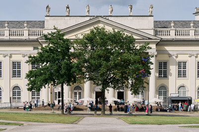 Das Fridericianum im Sommer von Au&szlig;en. Menschen sitzen auf der Terrasse vor dem Museum.