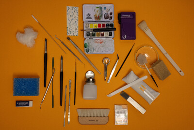 verschiedene Instrumente und Materialien der Restaurierungsarbeit präsentiert auf einer orangefarbenen Fläche