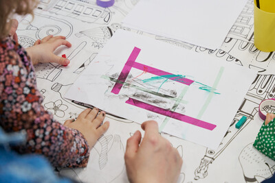 Ein Kind und eine erwachsene Person von hinten, die ein (vom Kind gebasteltetes) Bild ansehen.