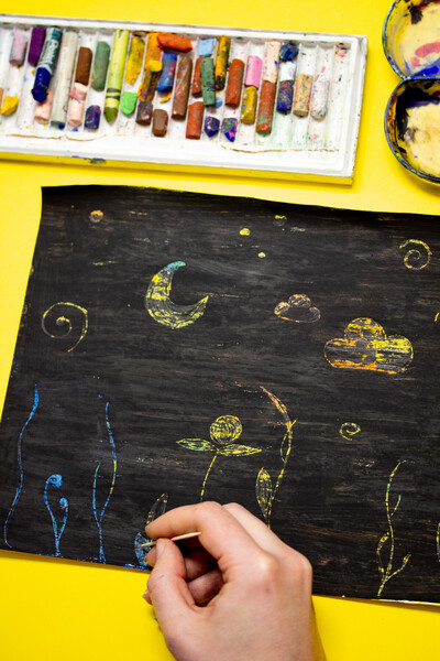 Foto einer Hand von oben, die mit einem Zahnstocher ein Motiv kratzt.