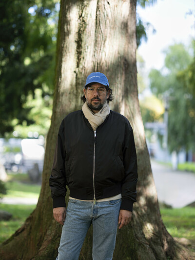 Mario García Torres steht vor einem großen Baum. Er trägt eine blaue Kappe und eine schwarze Jacke mit Reissverschluss.