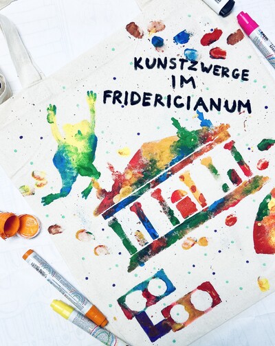 A photo of a colorfully painted cloth bag with “Kunstzwerge im Fridericianum” written on it.