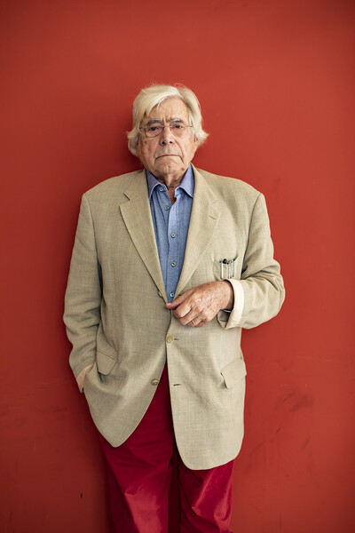 Photo of Bazon Brock posing in front of a red wall