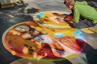 A man is sitting on the floor. He draws a colorful picture on the floor.