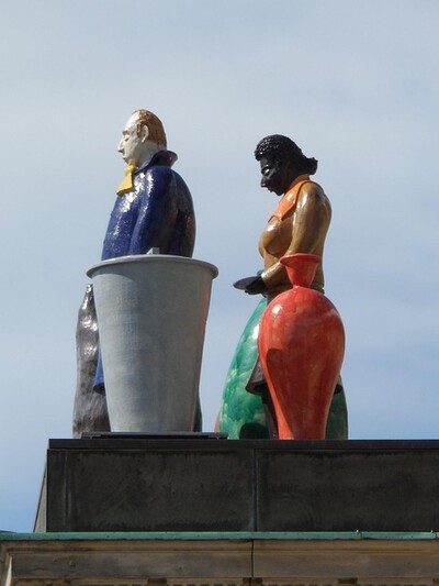 Bunte Figuren stehen auf einem Dach. Es sind große Kunstwerke aus hartem Material.