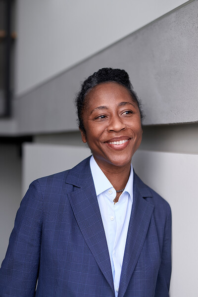 Naomi Beckwith lehnt an einer Wand. Sie lächelt.