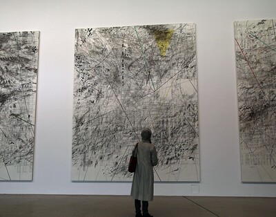 Eine Person steht vor einem großen Kunstbild. Das Bild hängt in einem Museum oder einer Ausstellung.