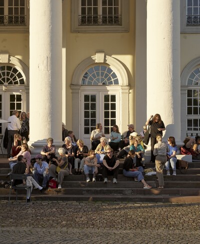 Viele Menschen sitzen in der Sonne auf den Treppen vor dem Museum Fridericianum.