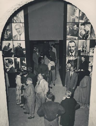 Historische Schwarzweißaufnahme. Menschen unterschiedlichen Alters betreten die Ausstellungsräume