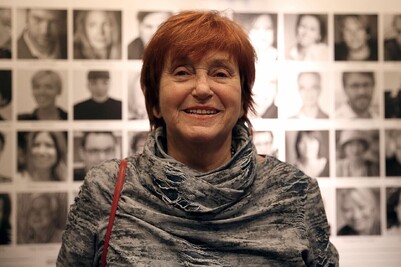 VALIE EXPORT, fotografiert beim &Ouml;sterreichischen Filmpreis 2013. Sie l&auml;chelt in die Kamera, vor einer Wand mit schwarz-wei&szlig;en Portr&auml;tfotos.