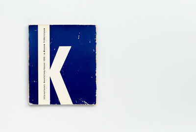 Rückseite des Katalogs der ersten documenta 1955. Die Gestaltung zeigt ein großes weißes „K“ auf blauem Grund. Am linken Rand verläuft vertikal der Schriftzug „Internationale Ausstellung Kassel 1955 im Museum Fridericianum“ in weißer Schrift.
