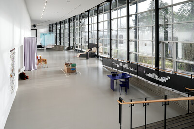 Innenansicht der documenta Halle mit großer Fensterfront. Man sieht einen Teil der Treppe, im Raum stehen verschiedene Objekte.