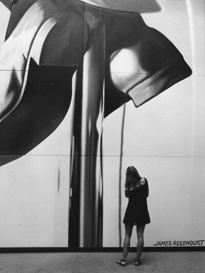 Eine Frau steht vor einem großen Kunstwerk, welches das ganze Bild ausfüllt.