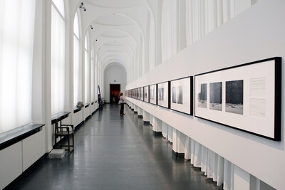 View of an exhibition hallway with black and white photographs in white frames on the wall.