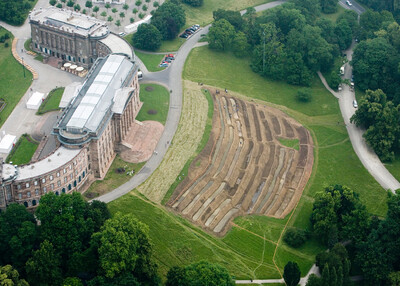 Aerial view of Wilhelmshöhe Palace with a large-scale work of earth art on the adjacent meadow.