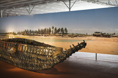 Boat made from old canisters in front of a large-format photo of a tropical beach landscape.
