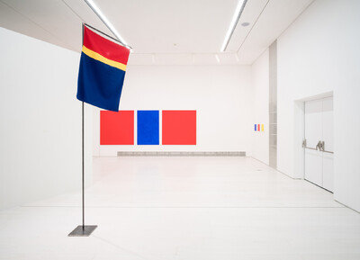 Blick in einen weißen Galerieraum mit einer skulptural installierten Fahne und monochromen Farbflächenbildern in Rot und Blau.