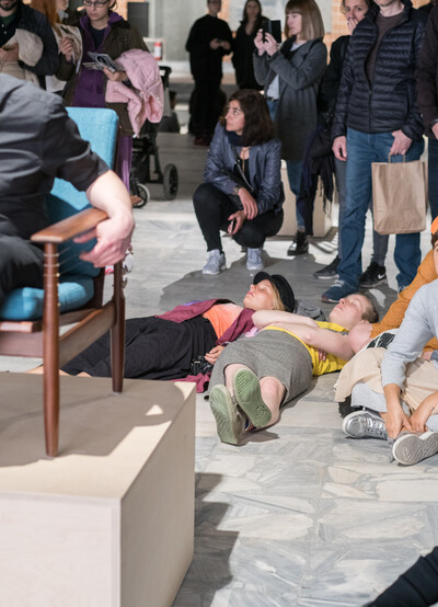 Mehrere Menschen sitzen und liegen auf dem Boden in einem Ausstellungsraum.