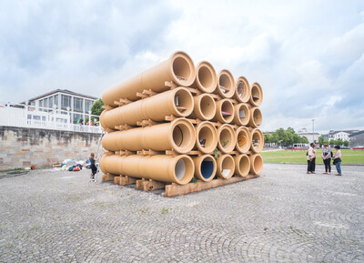 Ein Kunstwerk im Außenraum aus Abwasserrohren die gestapelt wurden. Die Rohre sind begehbar und jedes Rohr hat unterschiedliche Inhalte.