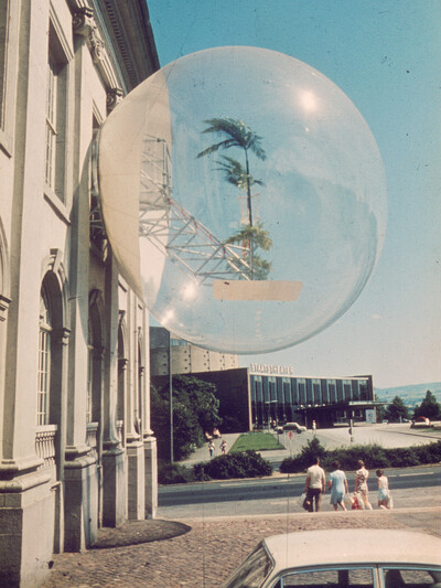 Seitenansicht des Fridericianum mit Blick auf das Staatstheater. An der Fassade des Fridericianum befindet sich eine Installation: Eine großer, transparenter Ball mit einer in den Ball ragenden Konstruktion aus Metall und Palmen
