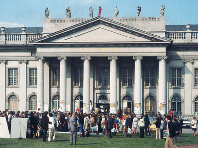 Vorderansicht des Fridericianum. Auf dem Vorplatz stehen viele Menschen. Die Säulen der Portkus sind mit teilweise Papier beklebt.