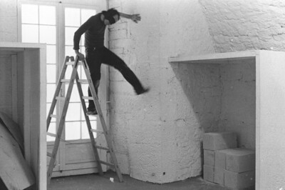 Ein Mann steht in einem geschlossenen Raum mit verbundenen Augen auf einer Leiter. Er stützt sich dabei mit seiner Hand an der Wand ab.