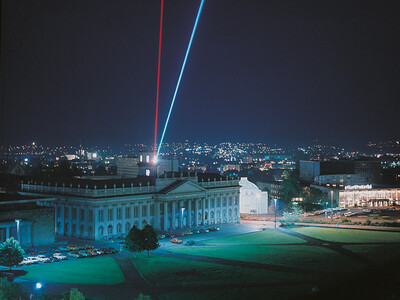 Das Fridericianum und die Stadt Kassel bei Nacht. Zwei Strahlen leuchten in den Himmel.