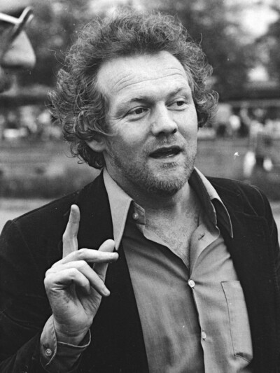Ein Portait des Künstlerischen Leiters, der die rechte Hand hebt und aufzeigt.