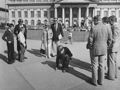 Vor dem Fridericianum stehen mehrere Personen um einen Menschen der auf dem Boden kniet.