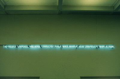 Eine Neonarbeit mit dem englischen Text „This object, sentence, and work completes itself while what is read constructs what is seen.“ ist an einer Wand installiert.
