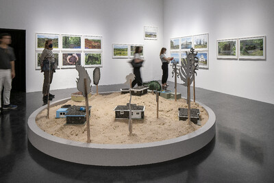 Auf dem Bild ist eine Installation zu sehen. In einem Kreis aus Sand stehen Modellhäuser und stilisierte Bäume.