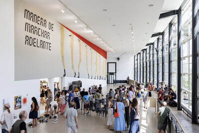 In de lichtdurchfluteten documenta Halle bewegen sich zahlreiche Besuchende. Ein großflächiger Schriftzug dominiert eine Wand als zentrales Element.