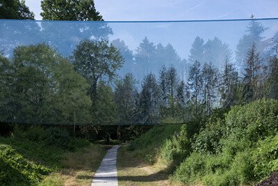 Eine großflächige, halbtransparente Stoffinstallation ist zwischen Bäumen gespannt. Sie reflektiert die umgebende Waldlandschaft und erzeugt eine optische Illusion.