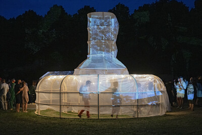 Eine leuchtende Skulptur mit Projektionen, umgeben von Besuchenden bei Nacht.