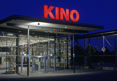 Die documenta Halle bei Nacht. Auf dem Dach über dem Eingang steht in großen roten Leuchtbuchstaben "Kino".