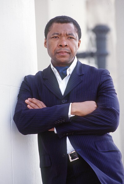 Porträt von Okwui Enwezor, künstlerischer Leiter der documenta 11, im Anzug mit verschränkten Armen.