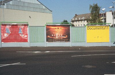 Plakatwand mit gelbem Plakat zur documenta 11, daneben Werbeplakate.
