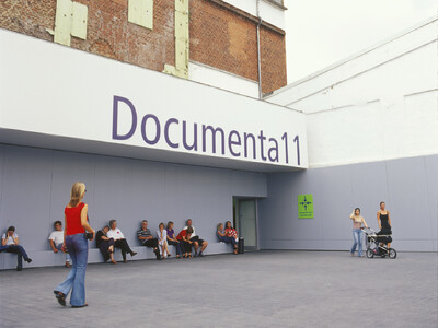 Ansicht des Eingangs zur documenta 11 mit Besucher*innen auf einer Bank vor der Fassade der Binding-Brauerei.