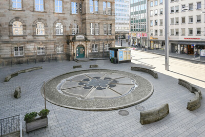 Ein runder Brunnen. In seiner Mitte befindet sich ein mit Gittern abgedecktes Loch. Das Wasser stürzt in die Tiefe.